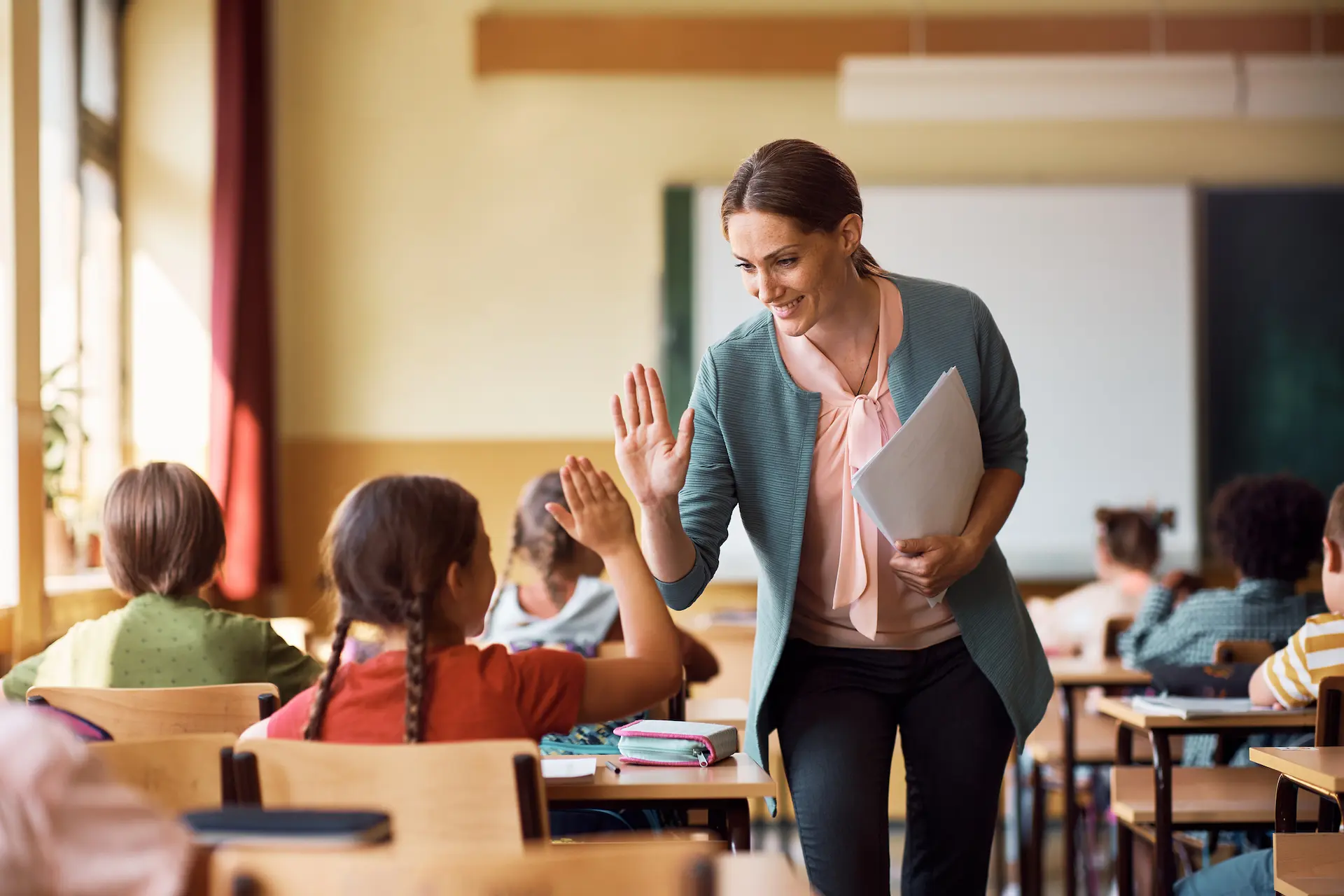 Happy teacher and schoolgirl giving high five during class at school