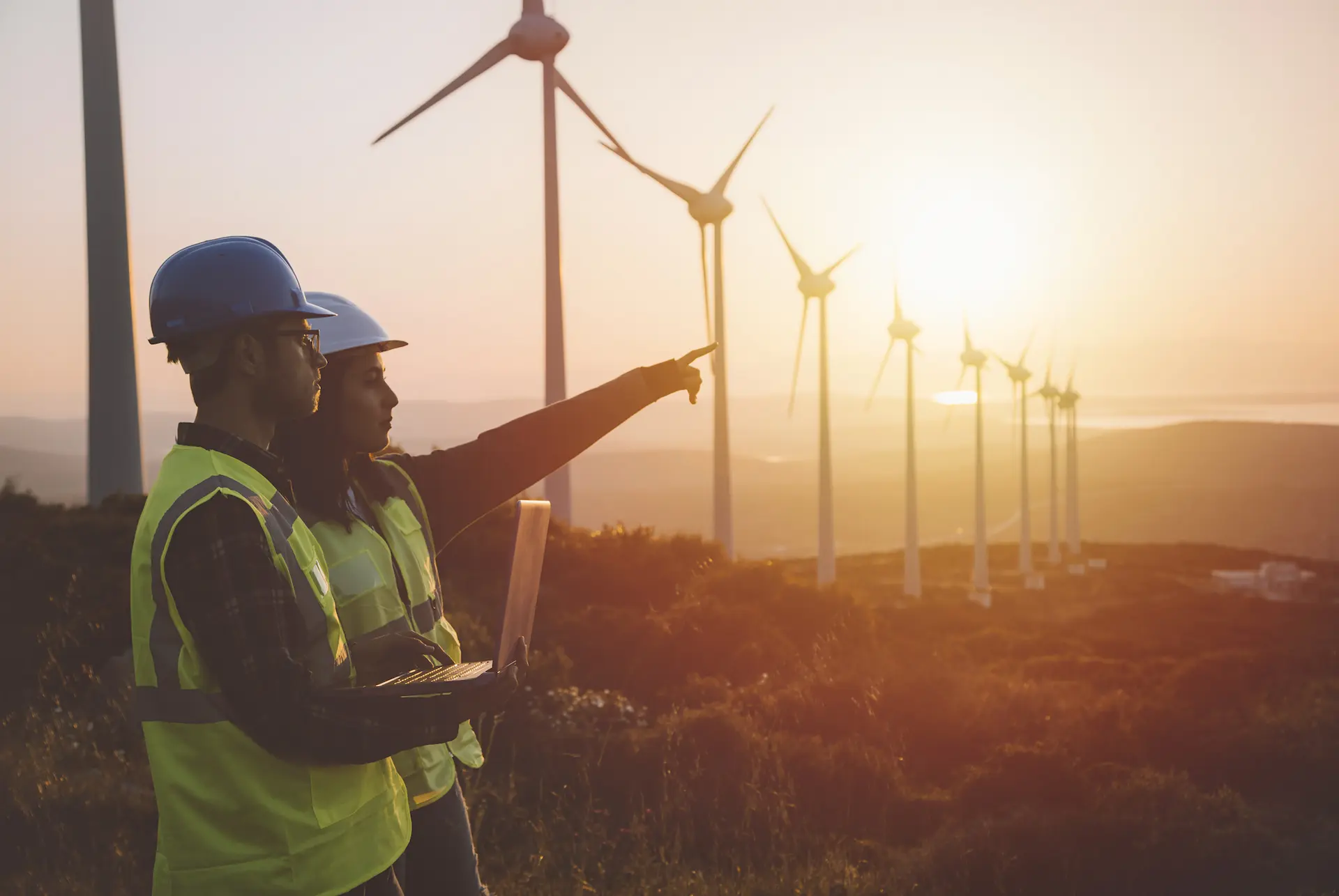 Young maintenance engineer team working in wind turbine farm at sunset