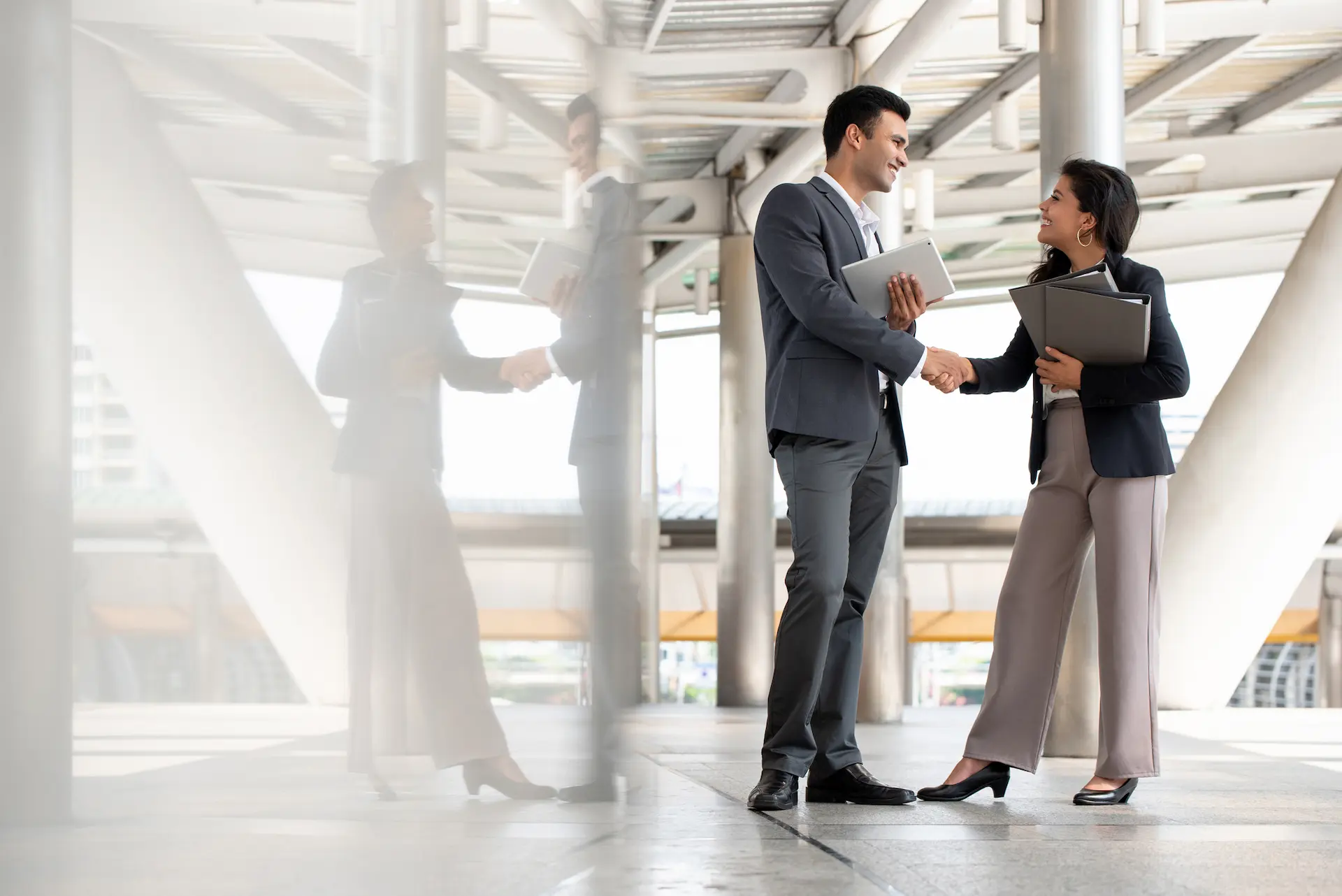 Indian businessman greeting and making handshake with a businesswoman outdoors in city walkway